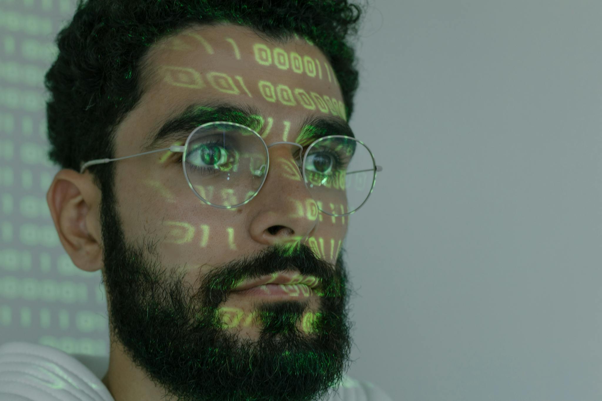 A bearded man with digital binary code projected on his face, symbolizing cybersecurity and technology.